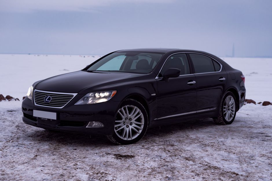 Sleek black Lexus LS 460 parked in a snowy field with glowing headlights.